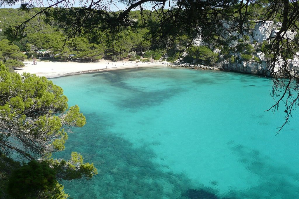 Turquoise waters of Cala Macarella cove in Menorca seen from the cliffside access path.