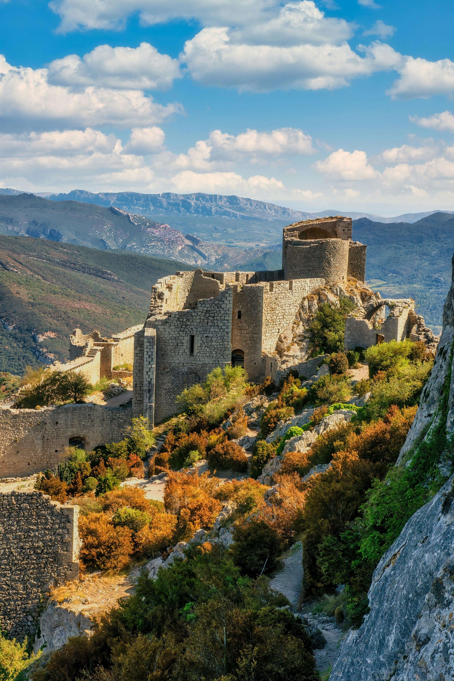 Car hire Toulouse Airport on the road below the Cathar castle of Peyrepertuse on a limestone ridge in the Corbières hills with valley views and clear skies.: The Cathar castles of the Corbières are among the most dramatically positioned fortifications in Europe. Peyrepertuse sits on a limestone ridge at 800 metres and is accessible by hire car from Toulouse Airport in under two hours.