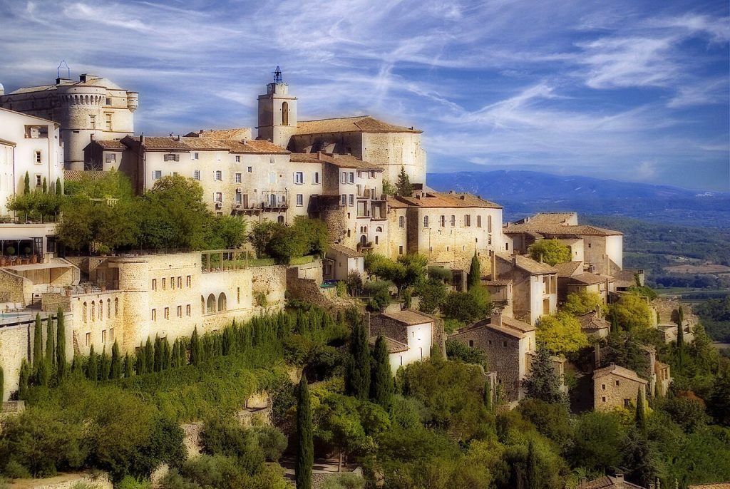 The village of Gordes perched on a steep limestone ridge above the Val de Sault in golden late afternoon light with the valley and distant Luberon plateau visible below.