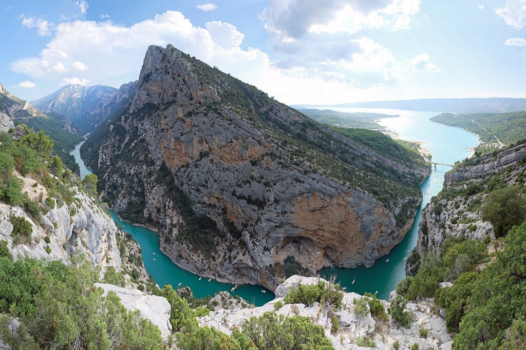 The Gorges du Verdon with turquoise river water winding through 700-metre limestone canyon walls with the D952 south rim road visible above and clear blue Provencal sky.