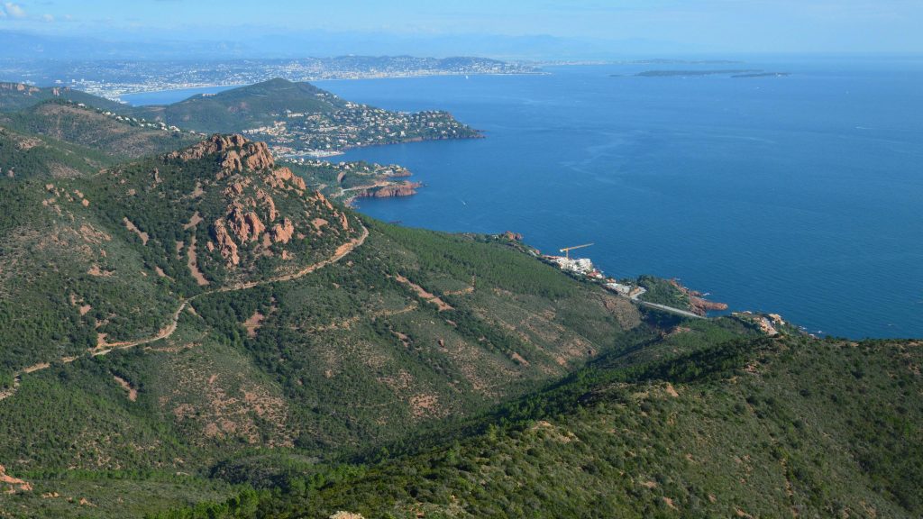 Red porphyry cliffs of the Massif de l'Esterel rising above turquoise Mediterranean water on the Corniche d'Or N98 between Theoule-sur-Mer and Saint-Raphael in afternoon light.