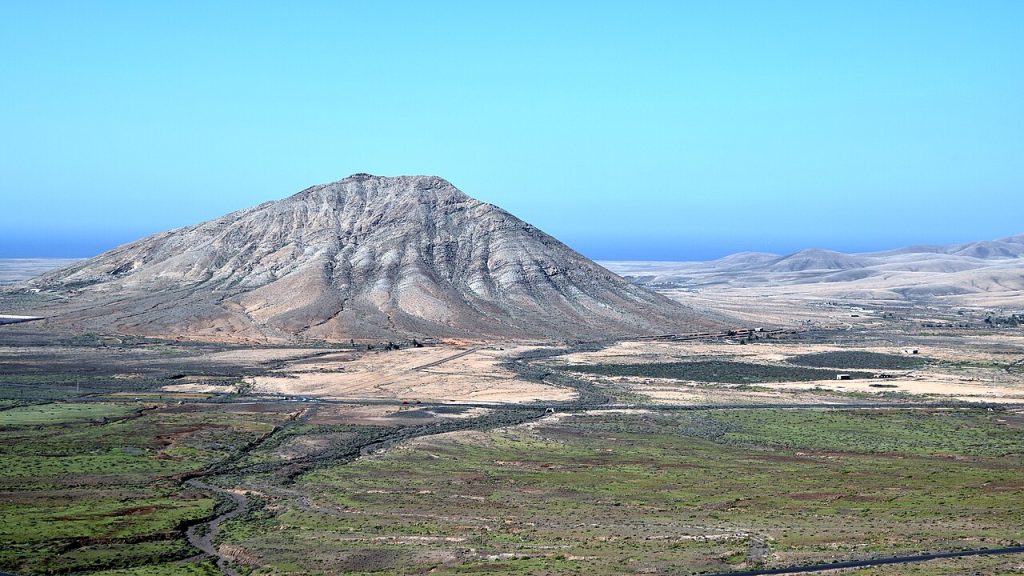 Drive 5 Tindaya sacred mountain Fuerteventura interior - volcanic rock rising from the northern plain with La Oliva church visible.