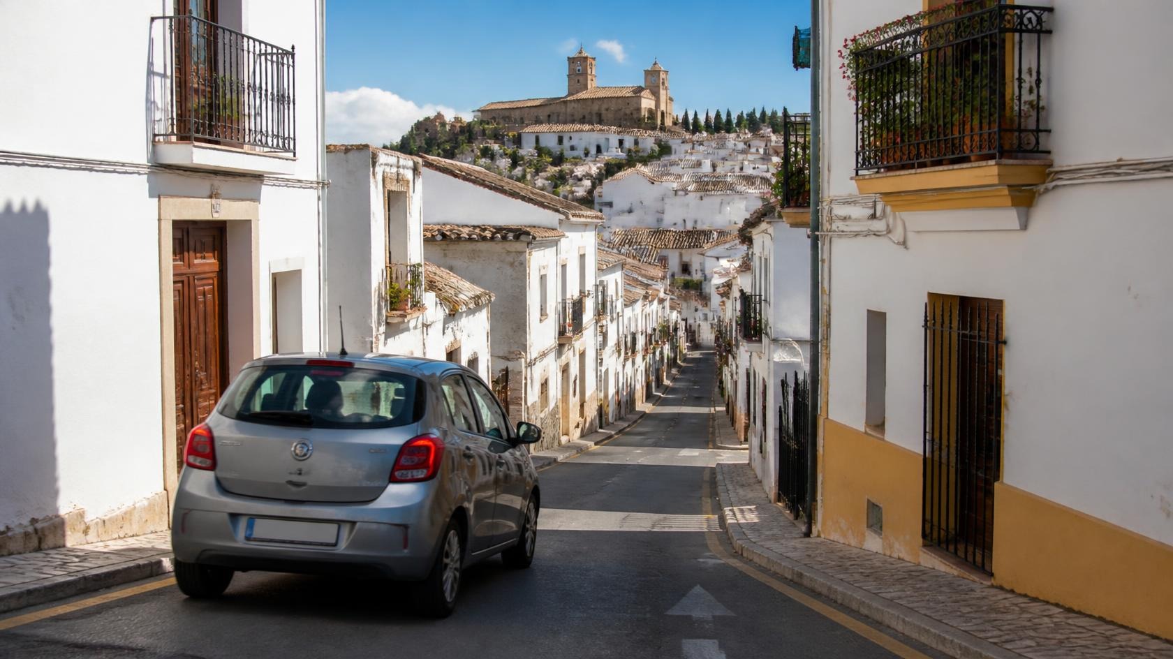 Kompakter Mietwagen in einer schmalen Gasse einer andalusischen Altstadt mit weißen Häusern und Balkonen